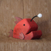 Whittled red wooden sculpture of an angler fish, with large cartoon type proportions. It has a light coming out of its head.