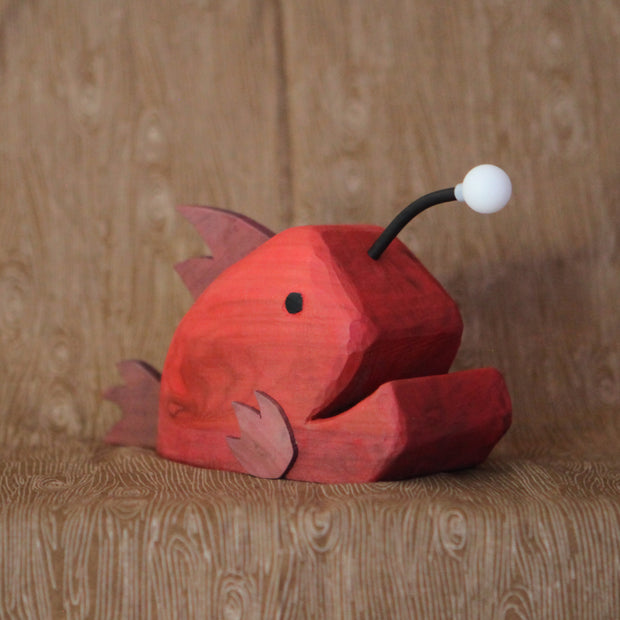 Whittled red wooden sculpture of an angler fish, with large cartoon type proportions. It has a light coming out of its head.