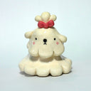 A small cream-colored ceramic figurine of a cute poodle or dog character with floppy ears, a pink bow on its head, and pink cheeks, set against a plain light background.