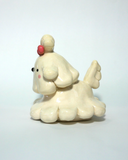 A small cream-colored ceramic figurine of a cute poodle or dog character with floppy ears, a pink bow on its head, and pink cheeks, set against a plain light background.