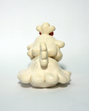 A small cream-colored ceramic figurine of a cute poodle or dog character with floppy ears, a pink bow on its head, and pink cheeks, set against a plain light background.
