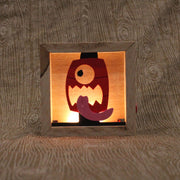 Wooden night light sculpture with a cut-out design of a face on a red lantern, with its tongue wildly out.