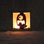 Wooden night light sculpture with a cut-out design of a face on a red lantern, with its tongue wildly out.