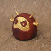 Wooden figure of a daruma figure with a golden face and head shaped like a Big Boss Robot.