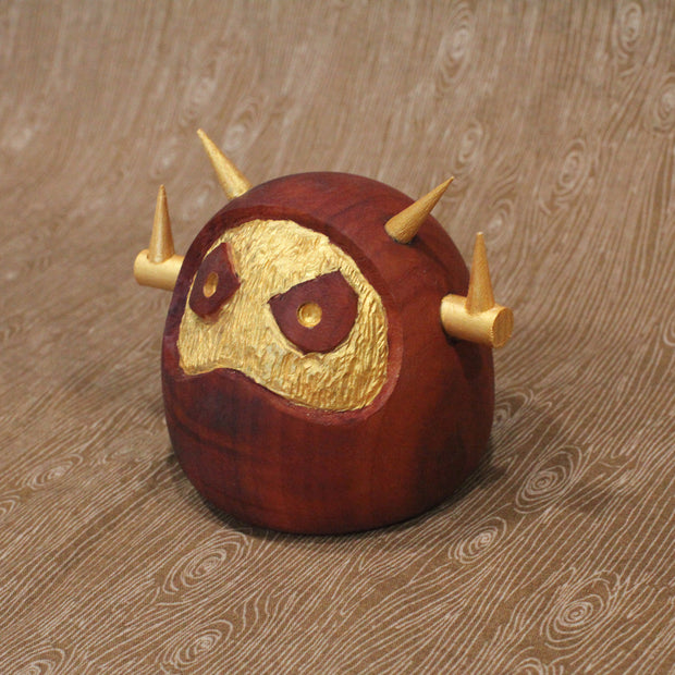 Wooden figure of a daruma figure with a golden face and head shaped like a Big Boss Robot.