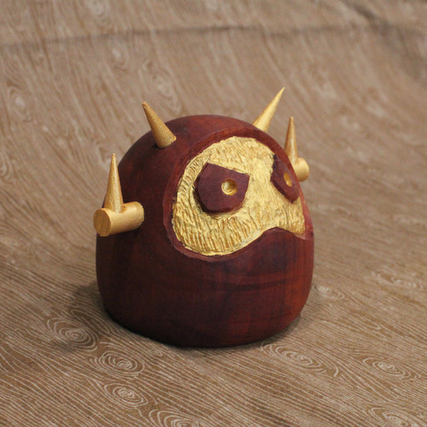 Wooden figure of a daruma figure with a golden face and head shaped like a Big Boss Robot.