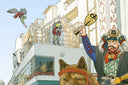Detail from panoramic illustration of of a person dressed like a decorated samurai riding on a large dog like a mount. People and animal creatures stand on large buildings behind them.