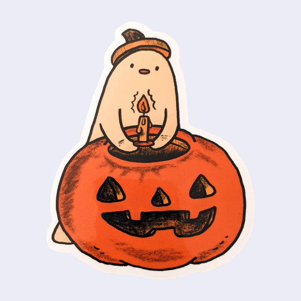Die cut sticker of a cream colored ghost putting a candle into a jack o lantern.