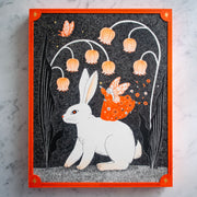 Black ink drawing with orange accent coloring of a large white rabbit, sitting between 2 even larger Lily of the Valley blossoms. Atop its back is a fairy in a bright orange dress, with flowers floating off of it. The piece is framed by a simple orange border.