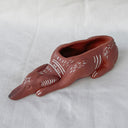 Ceramic sculpture of a long faced dog, laying flat with a large opening in its back for a shallow planter.