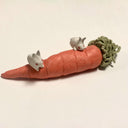 Colored porcelain sculpture of a carrot with lots of stringy greenery atop it, resting on its side. 2 small white rabbits with red eyes stand on top of it.
