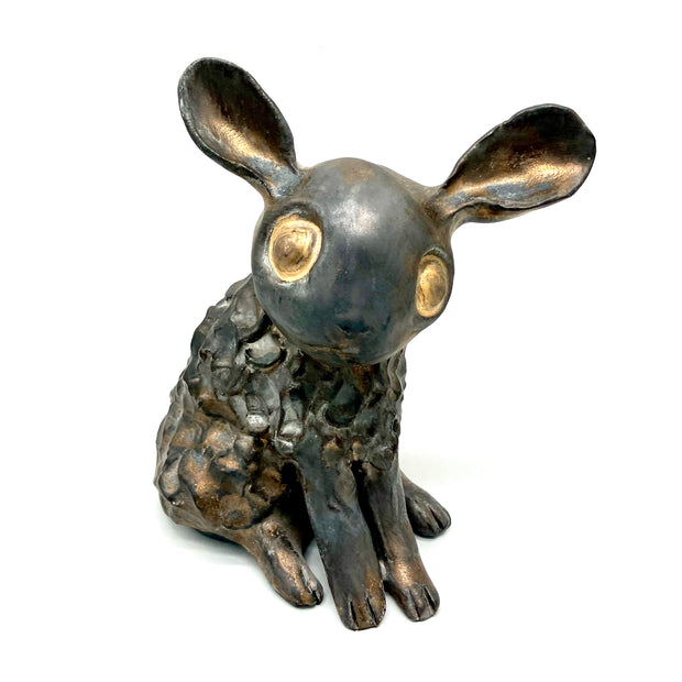 Bronze looking ceramic sculpture of a bunny with large gold eyes and large ears. Its body is fluffy alike to a sheep and it sits with its hands in front.