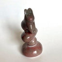 Stone sculpture of a stylized rabbit sitting atop of a pile of rocks, on a white background