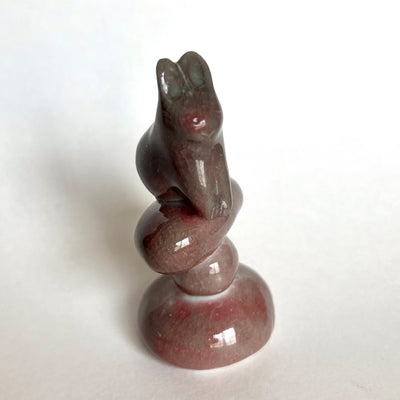 Stone sculpture of a stylized rabbit sitting atop of a pile of rocks, on a white background