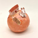 Small ceramic sculpture of a rounded orange sphere, with a white rabbit emerging out of it with a house behind it and a building buried into the ground.