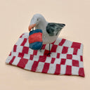 Ceramic sculpture of a seagull eating holding a bag of chips on a red checkered towel.