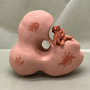 Pink ceramic sculpture with a smaller brown figure - a small child hugging a dinosaur.