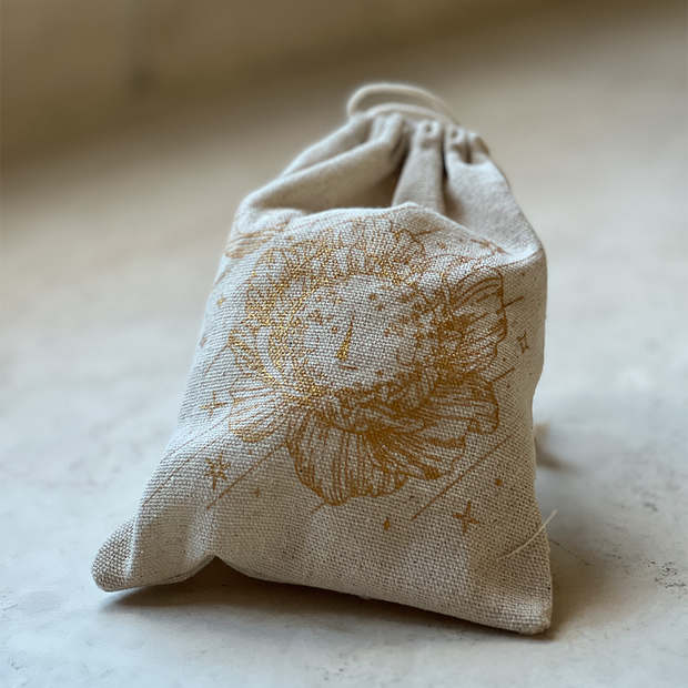 Closed cream colored linen bag with a graphic of a illustrated moonflower on the front in gold ink.