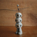 Painted whittled wooden sculpture of 3 eyeball stone monsters stacked atop of each other with an antenna on the top of its head.