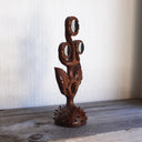 Whittled wooden sculpture of a statuesque plant, with only 2 leaves and 3 buds that have eyes on them. They all look off to the side and the plant is atop of a slightly spiked base. 