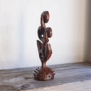 Whittled wooden sculpture of a statuesque plant, with only 2 leaves and 3 buds that have eyes on them. They all look off to the side and the plant is atop of a slightly spiked base. 