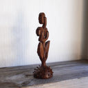 Whittled wooden sculpture of a statuesque plant, with only 2 leaves and 3 buds that have eyes on them. They all look off to the side and the plant is atop of a slightly spiked base. 