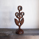 Whittled wooden sculpture of a statuesque plant, with only 2 leaves and 3 buds that have eyes on them. They all look off to the side and the plant is atop of a slightly spiked base. 
