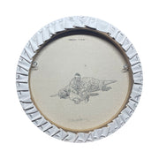 Back view of a circular canvas painting, featuring a line art style drawing of a man sitting on the ground with a knife next to a slain Godzilla.