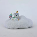 A small ceramic unicorn figurine with a pastel rainbow-colored tail and golden horn, sitting on a fluffy white cloud-shaped base against a plain light background.