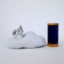 A small ceramic unicorn figurine with a pastel rainbow-colored tail and golden horn, sitting on a fluffy white cloud-shaped base against a plain light background.