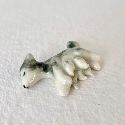 Glossy ceramic sculpture of a husky dog, laying down on its side with small shapes, like puppies, resting near her teat. 