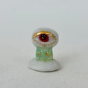 A small decorative figurine of a character with one large eye, a red pupil and a green cylindrical body. It is positioned on a white cloud-like base.