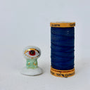 A small decorative figurine of a character with one large eye, a red pupil and a green cylindrical body. It is positioned on a white cloud-like base.