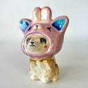 Glossy ceramic sculpture of a brown Shiba Inu sitting on the ground with glittery anime eyes. It wears a pink bunny hood hat.