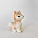 Small glossy ceramic sculpture of a brown and white shiba inu dog, sitting.