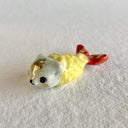 Glossy ceramic sculpture of a piece of shrimp tempura with a golden battered body and a white dog's head where the top of the shrimp would be.