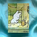 Artwork featuring a hand-drawn illustration of a white cat sitting at a bar with a beer mug, placed on a draped turquoise fabric background.
