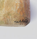 Close-up of a textured beige and gold painted surface with a black cursive signature reading 'madeleine' on a plain light background.