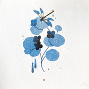 Blue illustration of a dragon fly on top of leaves with flower buds. 2 small ghost puppets hang from the leaves. Piece has subtle gold painted details.