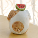 Clay sculpture of a round character, modeled to look like a dog without any arms or legs. Atop its head is an watermelon slice.