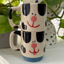 2 stackable cream colored mugs, one atop of the other. They have black spots and cute, cartoon faces to make them look like Dalmatian puppies. 