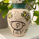 Cream colored vase with a teal green rim and black, teal and light green illustrations of dogs and nature elements, done in a cute simplistic style.