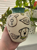 Cream colored vase with a teal green rim and black, teal and light green illustrations of dogs and nature elements, done in a cute simplistic style.