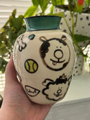 Cream colored vase with a teal green rim and black, teal and light green illustrations of dogs and nature elements, done in a cute simplistic style.