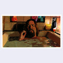 Person with long hair and beard lying in a bathtub with candles and a lamp in the background