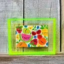 Painting of several colorful fruits with cartoon faces on them. Piece is framed in a fluorescent yellow color acrylic borderless frame.