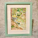 Loose style watercolor painting of a forest creek, with various plants growing nearby and casting their shadows into the water. Piece is in thin mint colored frame.