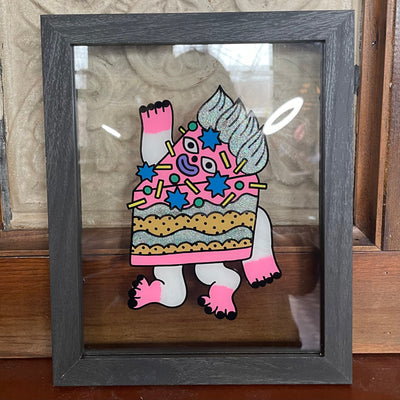 Painting on glass of a cartoon style cake with pink and silver glitter icing. It has sprinkles and a face, with arms and legs.