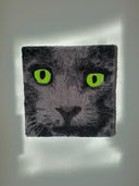 Tufted rug art of a close up of a gray cat's face, with bright green eyes and a wide eyed, closed moth expression. 