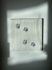 Rug tufting art of a white rug with 4 small gray cat paw prints.